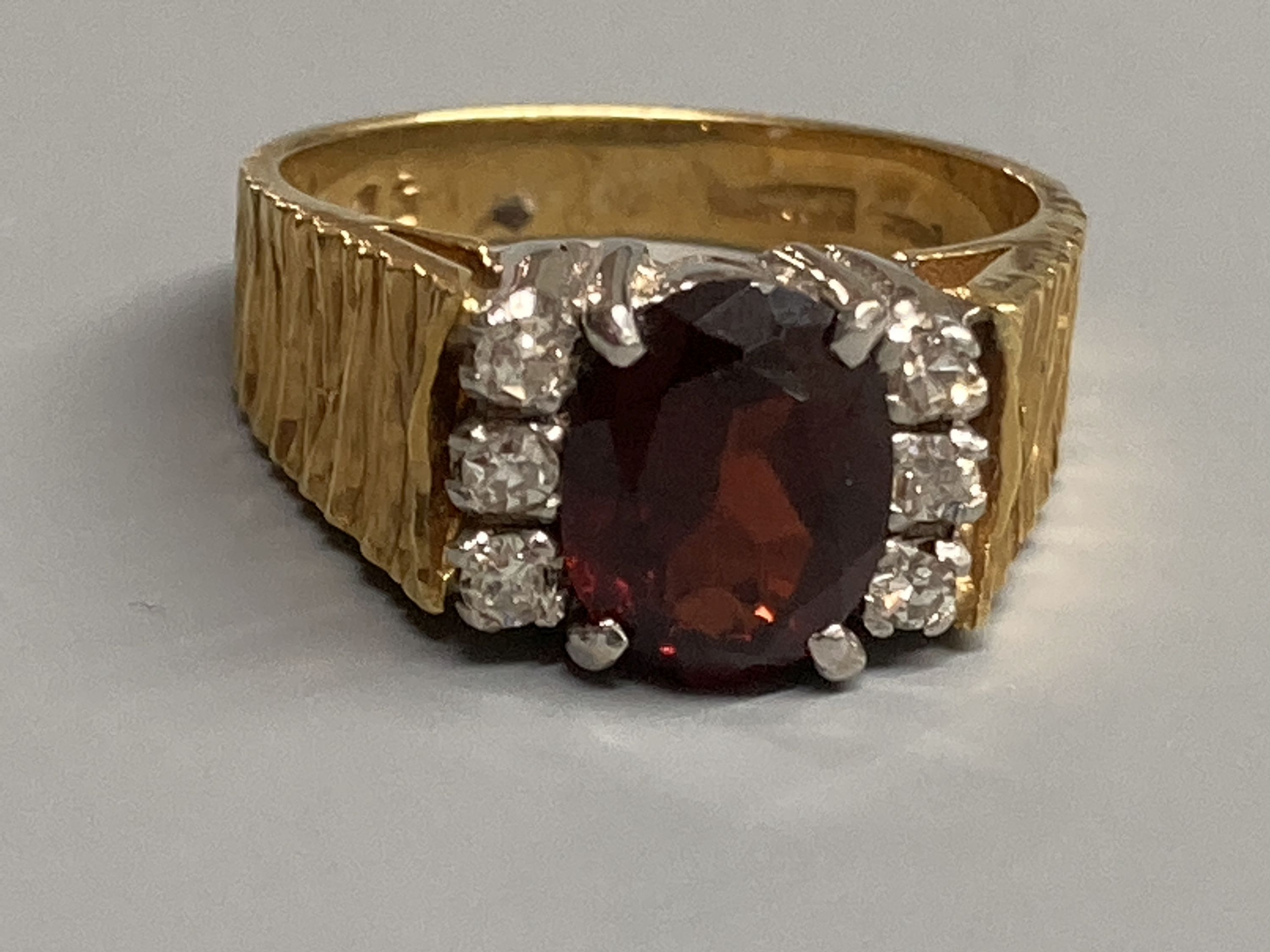 A 1970's 18ct gold, garnet and diamond cluster ring, with textured shoulders, size N/O, gross 7.9 grams.